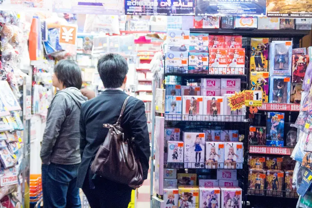 Deux clients vus de dos devant un rayon chargé de figurines en boîte, dans une boutique d'Akihabara à Tokyo