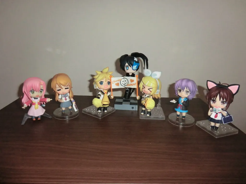 Sept Nendoroid de personnages différents alignés sur un meuble en bois, toutes à la même échelle